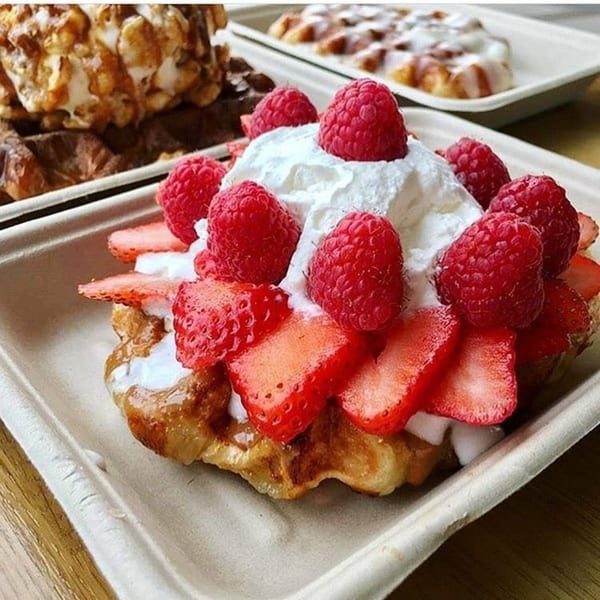 A waffle topped with whipped cream, fresh strawberries, and raspberries in a white container.