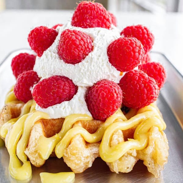 Waffle topped with lemon curd, whipped cream, and fresh raspberries on a silver tray.