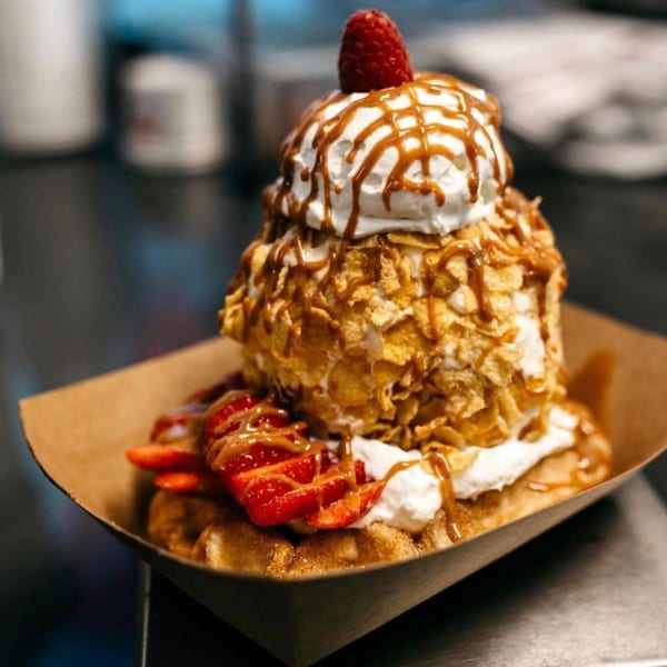 Waffle dessert with ice cream, cornflakes, whipped cream, caramel, strawberries, and a raspberry.