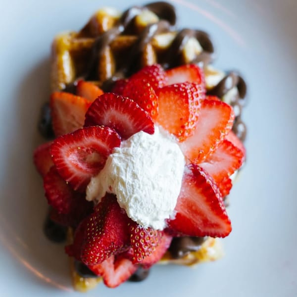 Golden waffle drizzled with chocolate, topped with fresh strawberries and whipped cream.