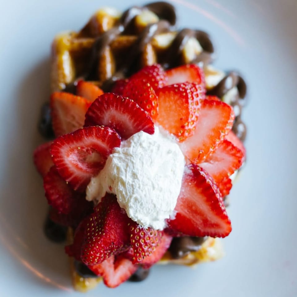 Golden waffle drizzled with chocolate, topped with fresh strawberries and whipped cream.