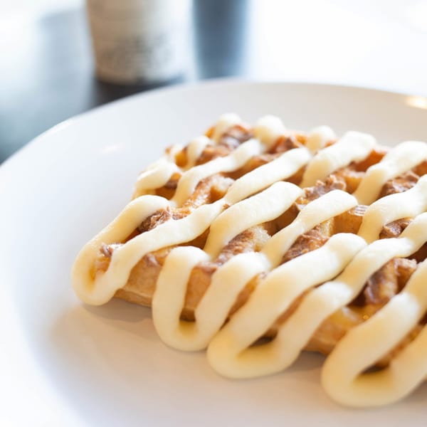 Close-up of a golden waffle drizzled with white icing, served on a white plate.
